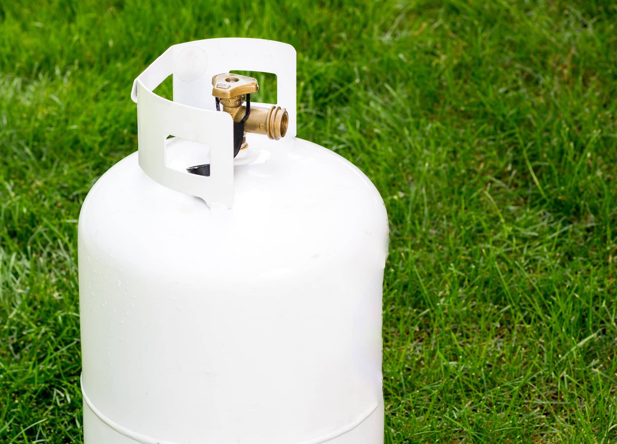 White propane tank with valve on top, placed on green grass outdoors.
