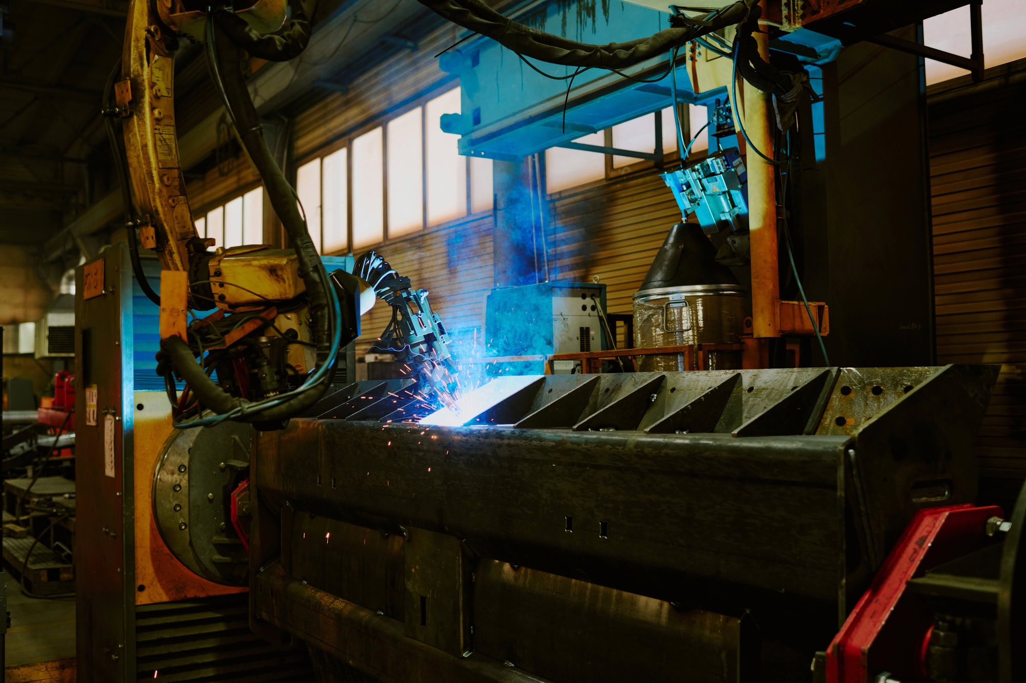 Industrial robot arm welding a metal beam in a factory setting.