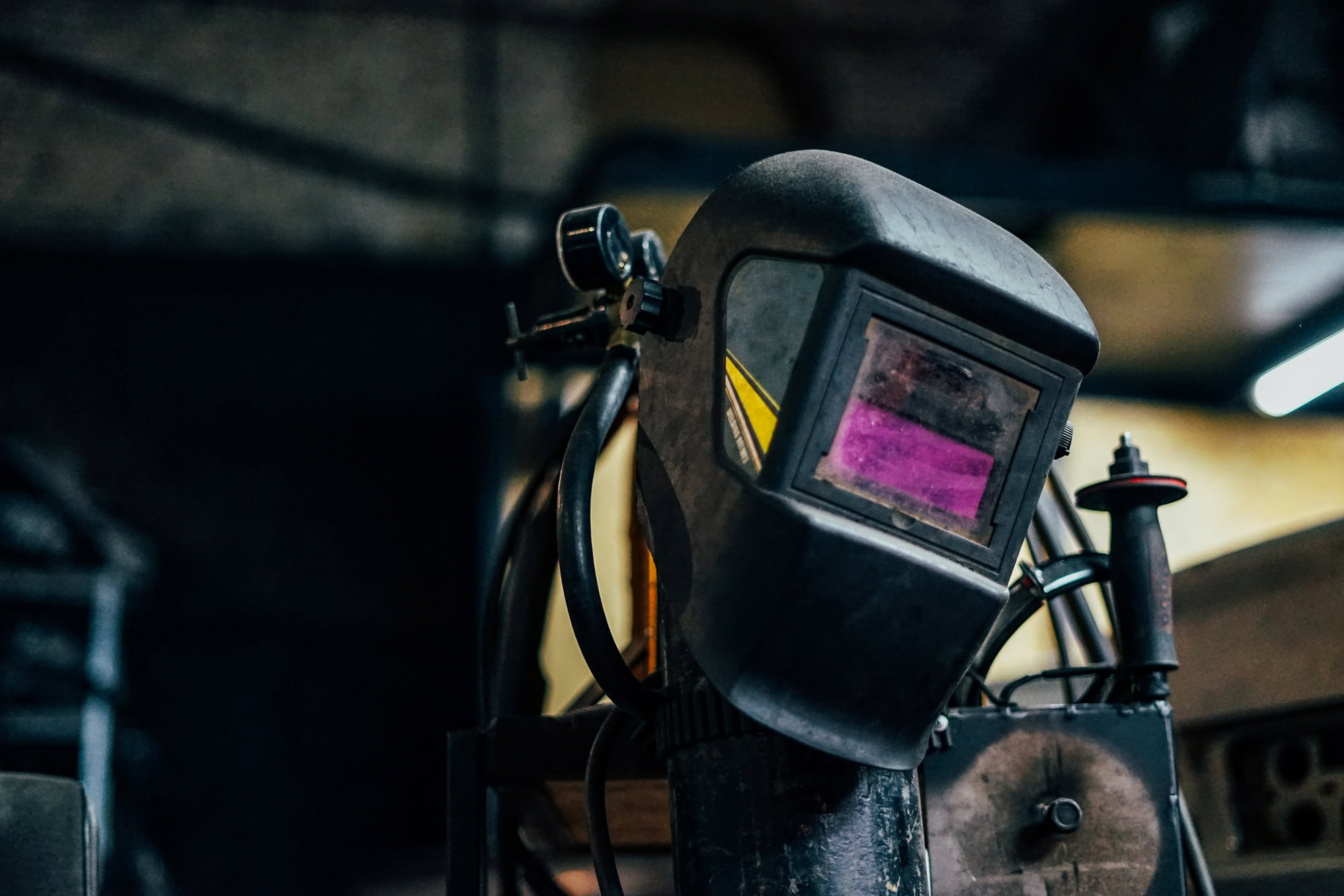 A welding helmet with a tinted visor resting in an industrial workshop setting.