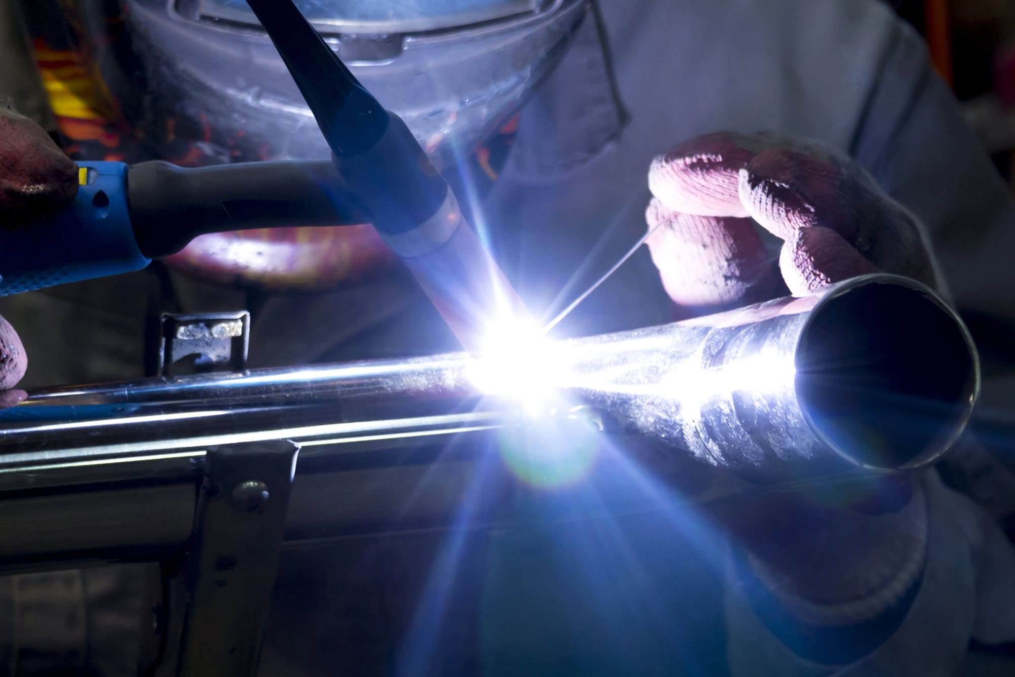 A person welding a metal pipe, creating a bright arc of light.