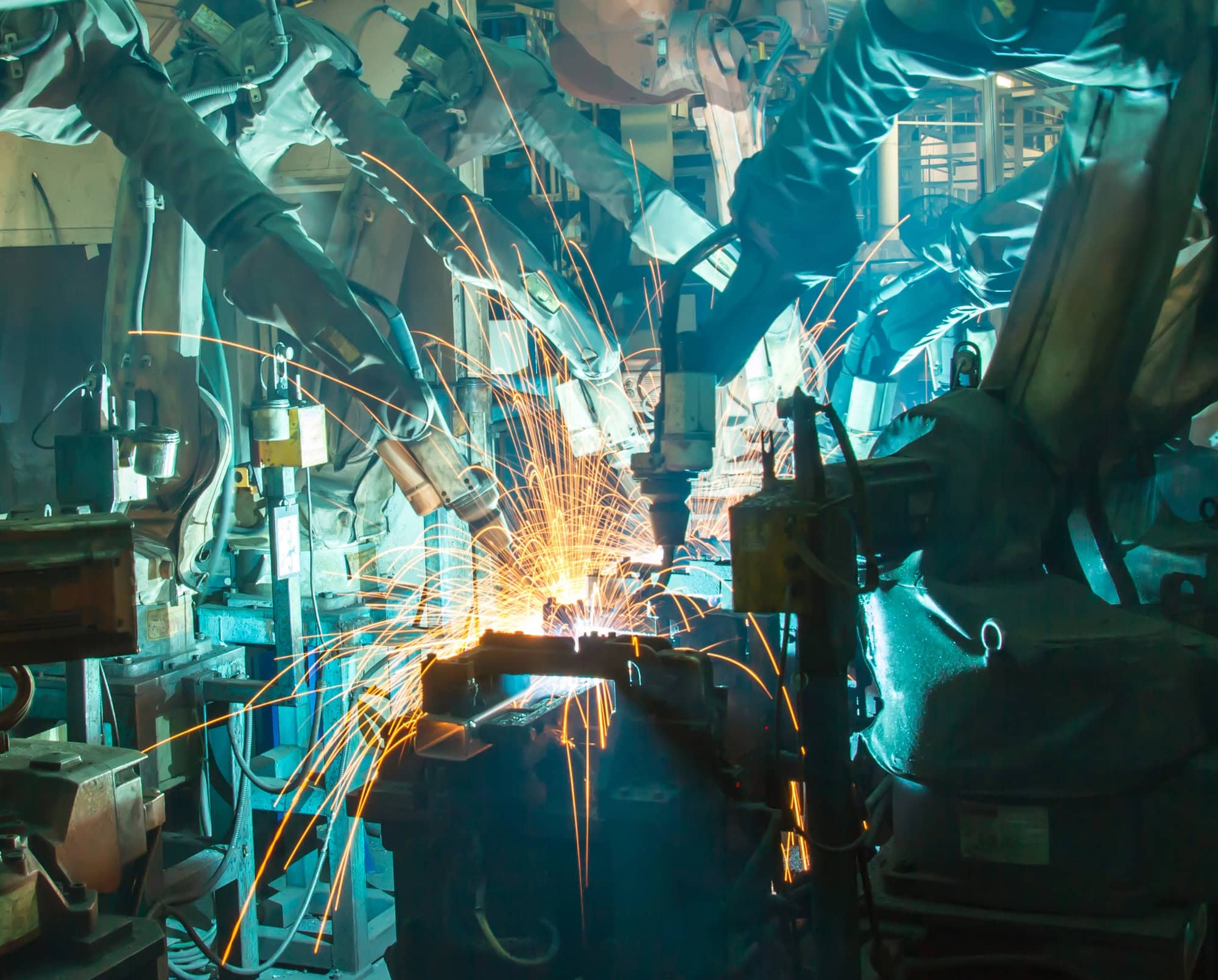 Industrial robots welding metal parts with sparks flying in a factory setting.