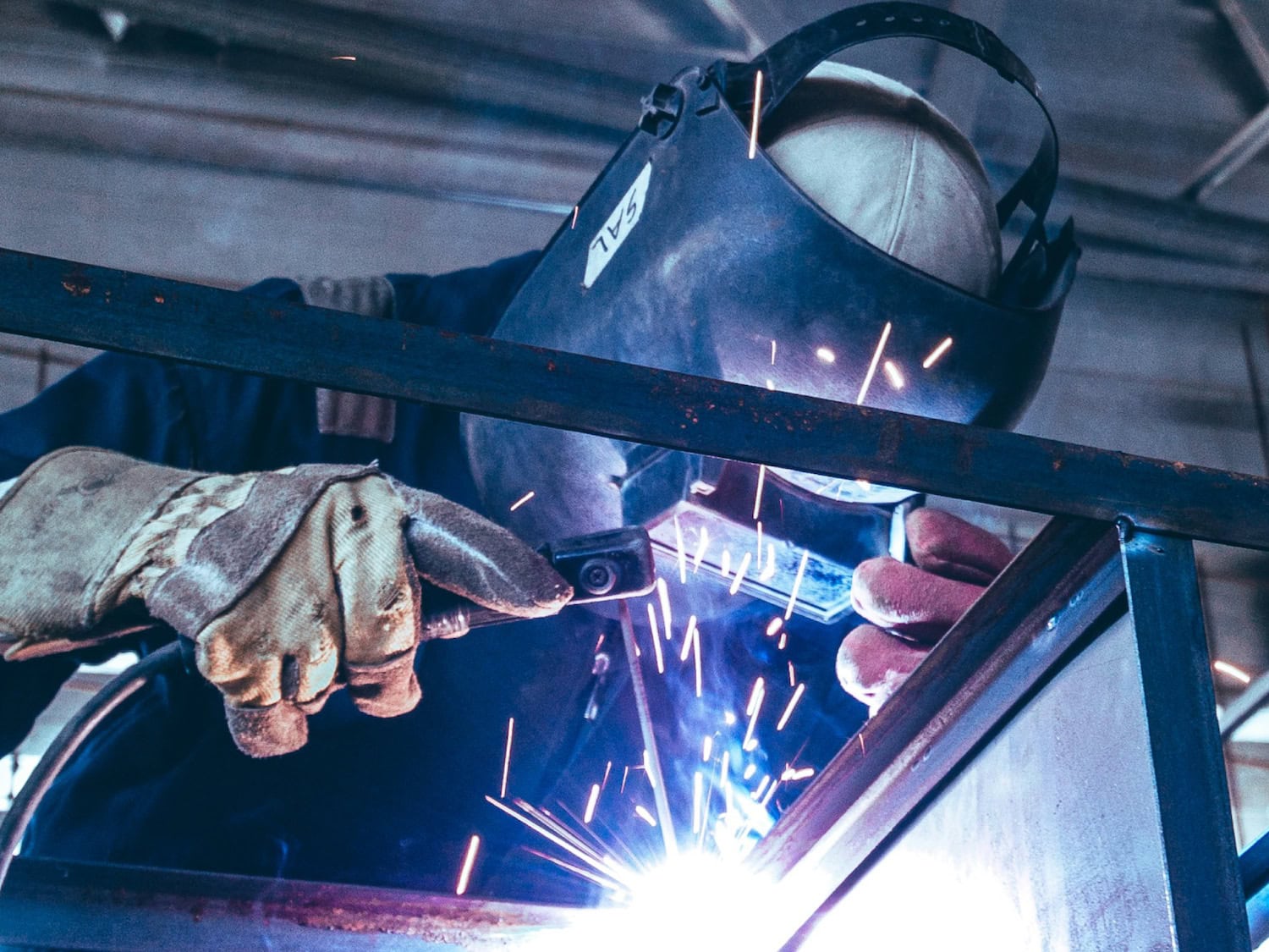Person welding metal while wearing protective gear.