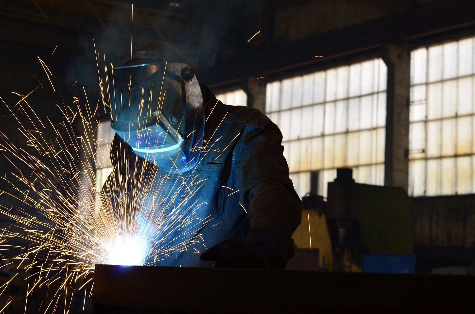 Person welding metal in a workshop, with bright sparks and protective gear visible.