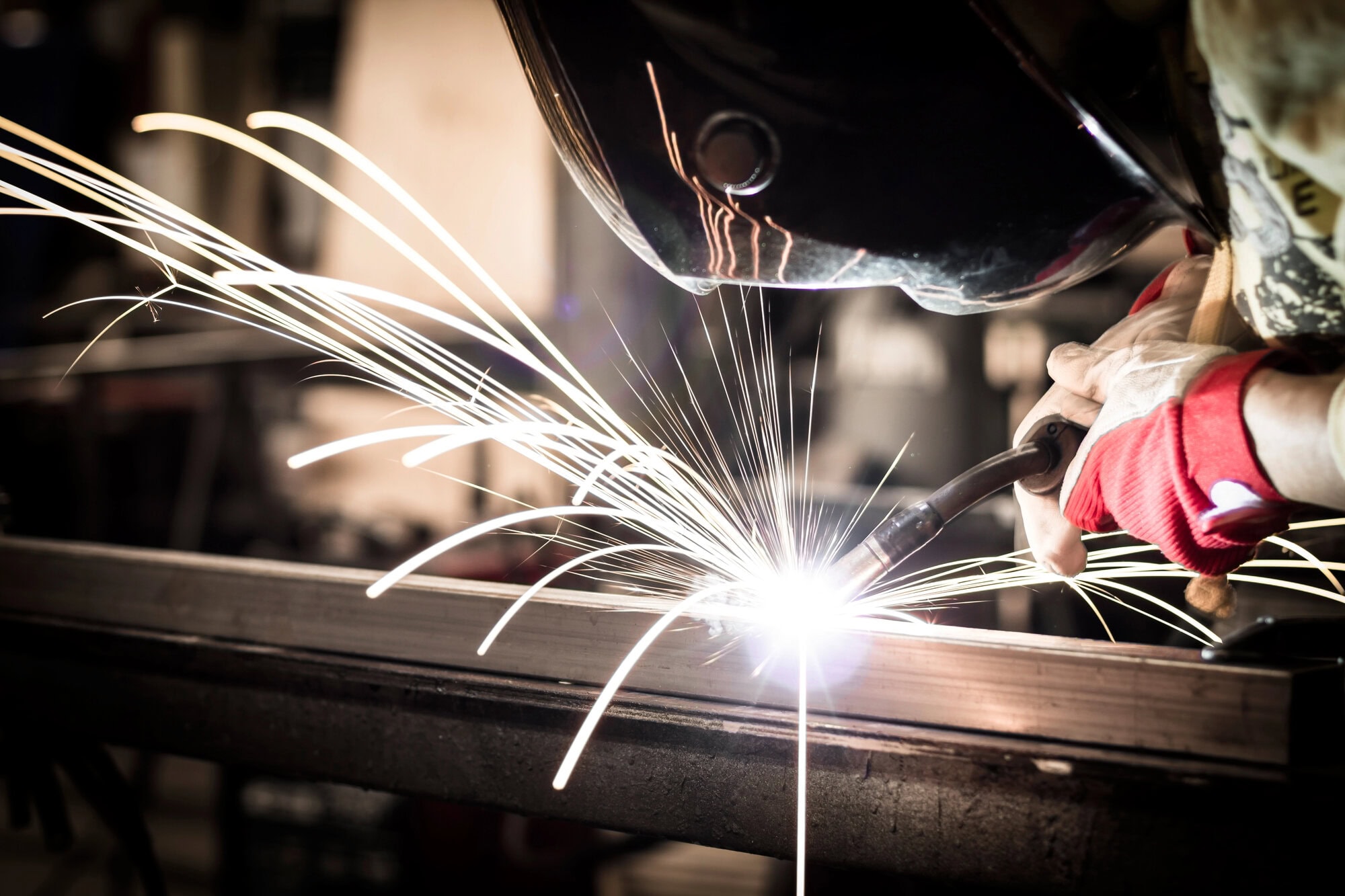Person welding metal, wearing protective gloves and helmet, with sparks flying.