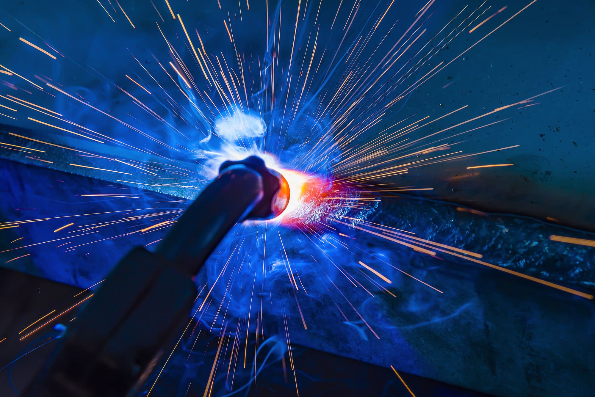 Close-up of a welding torch emitting sparks and blue smoke during metalwork.
