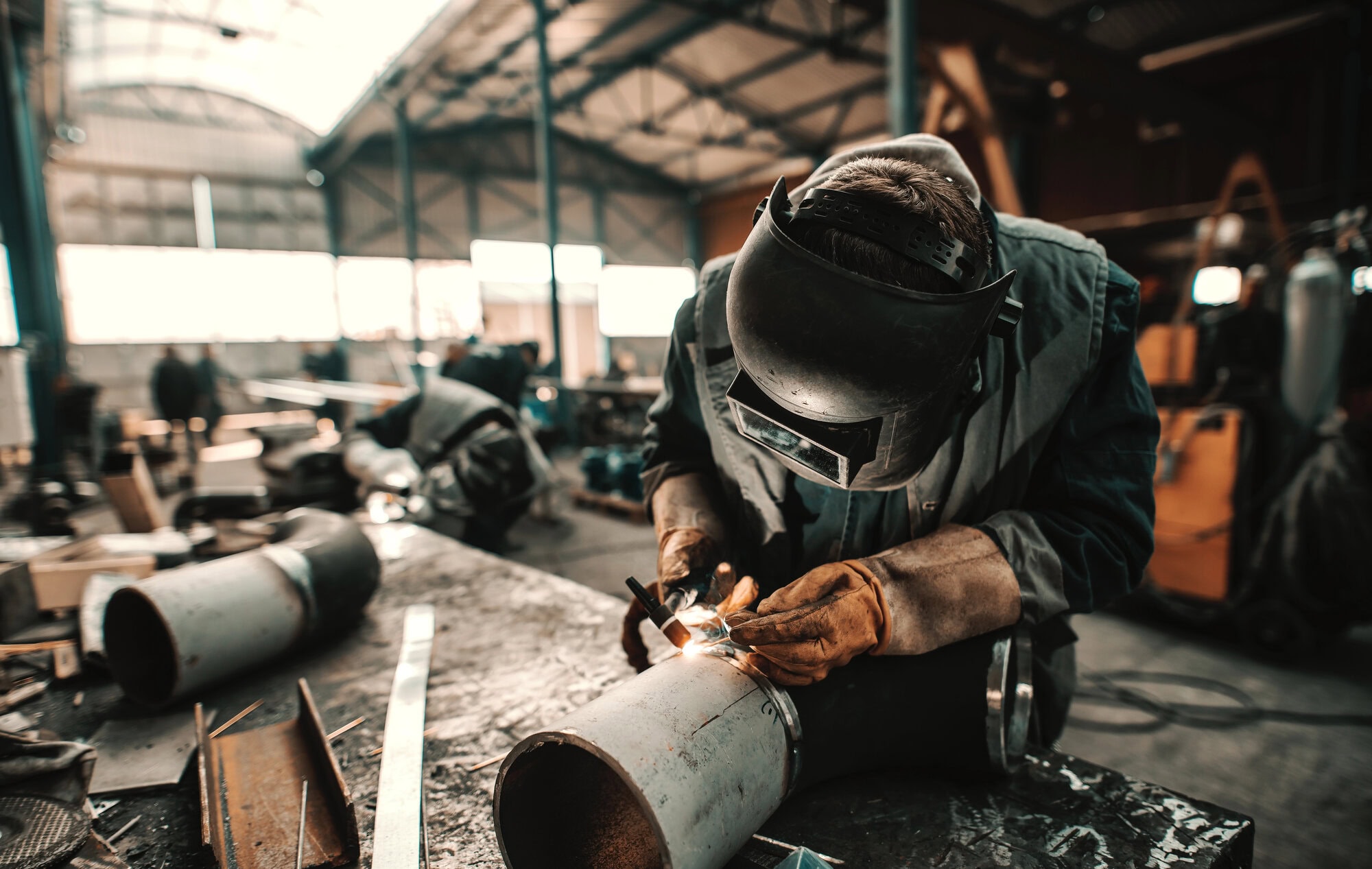 A worker in protective gear welds a metal pipe in an industrial workshop.