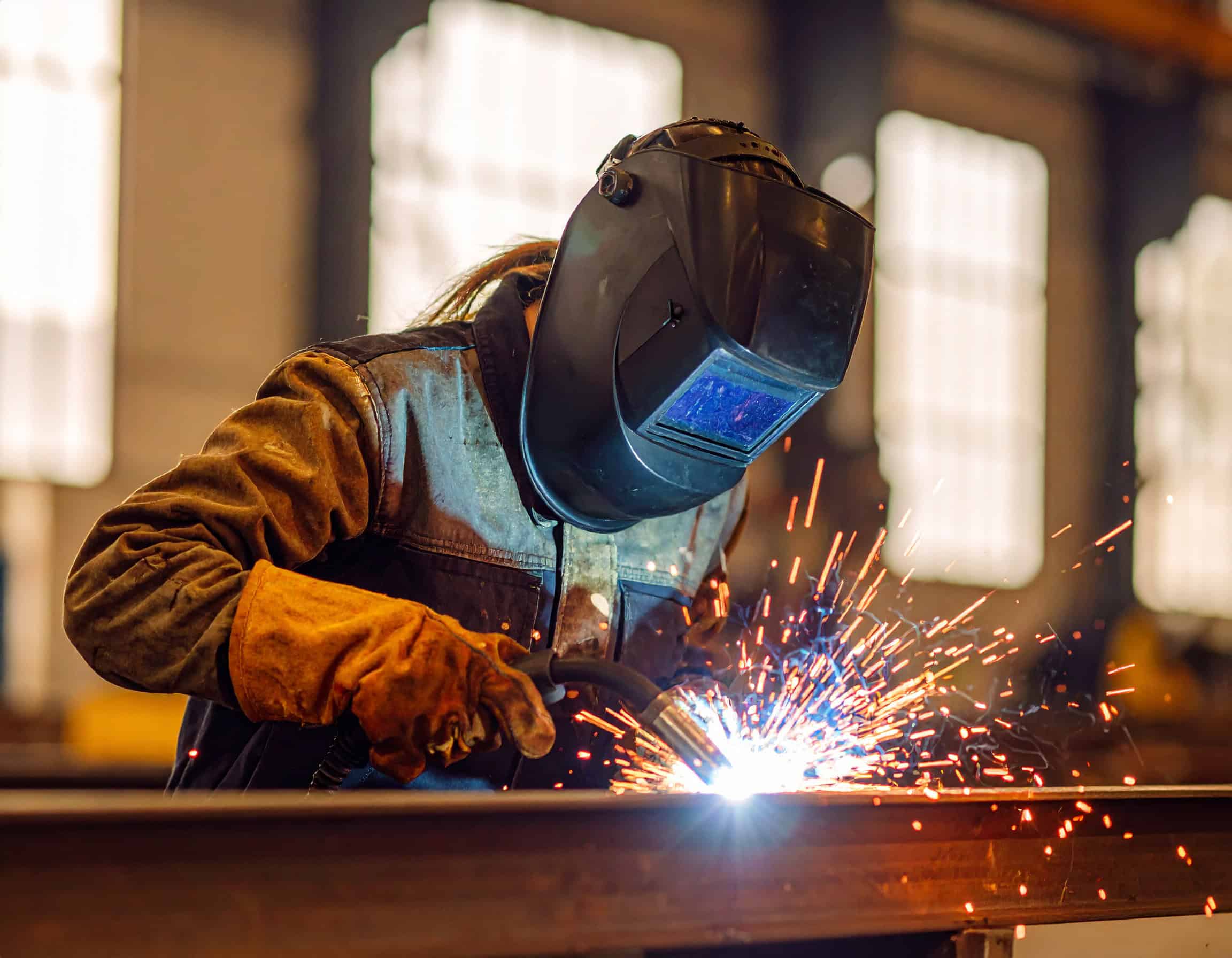 Person wearing a welding helmet welding metal, with bright sparks flying from the work area.