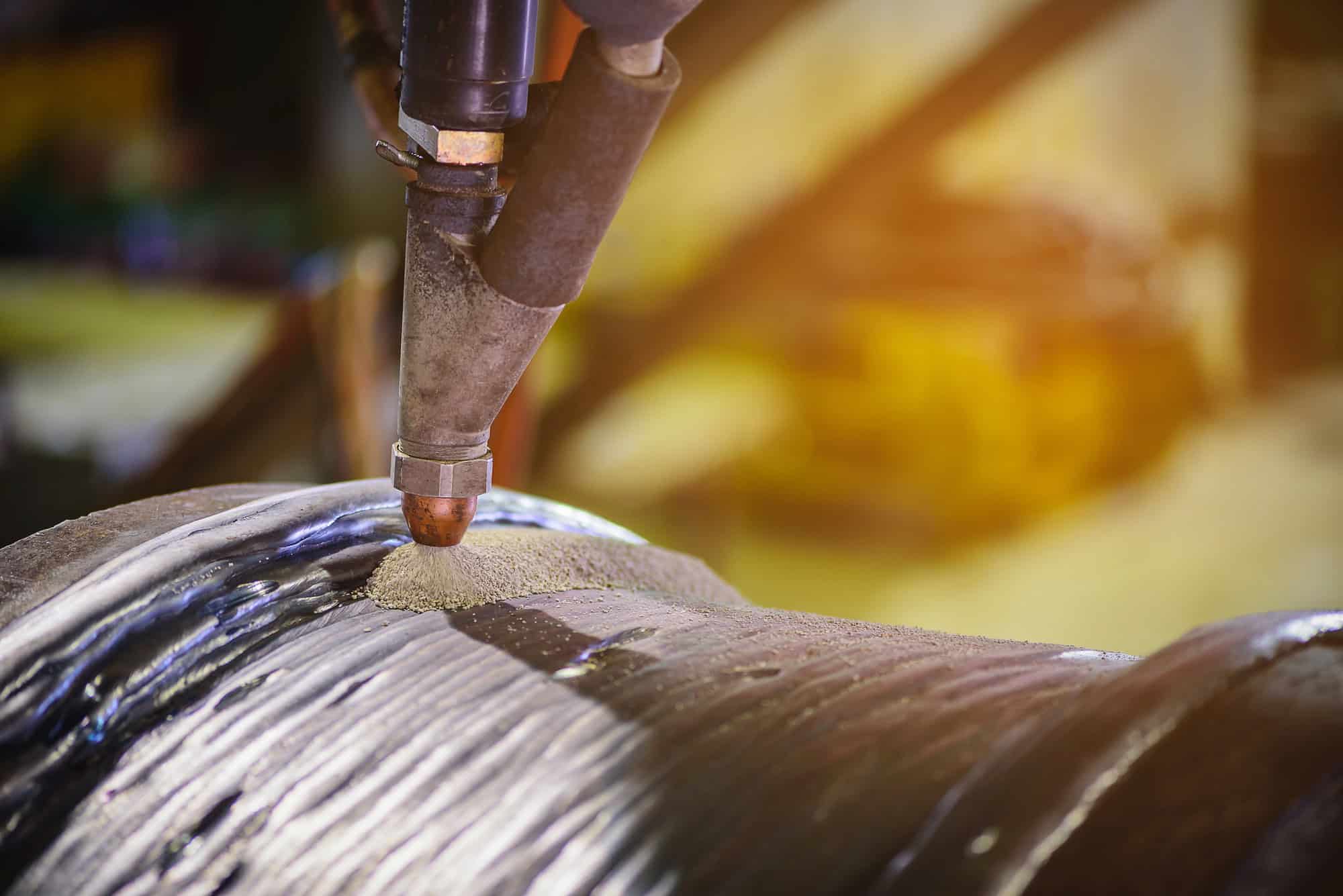Close-up of an industrial welding or metal additive manufacturing process on a curved surface.