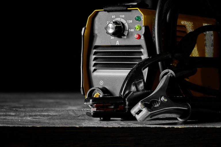 Close-up of a welding machine with cables and a clamp on a wooden surface.
