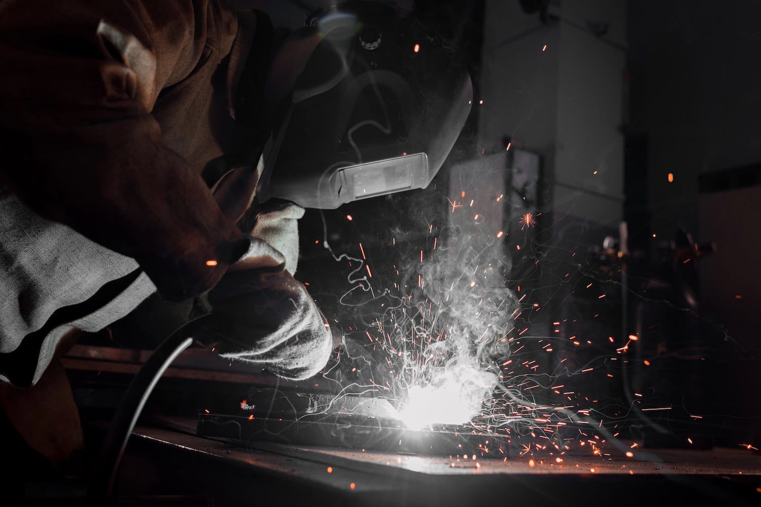 Person welding metal with protective gear, sparks and smoke visible.