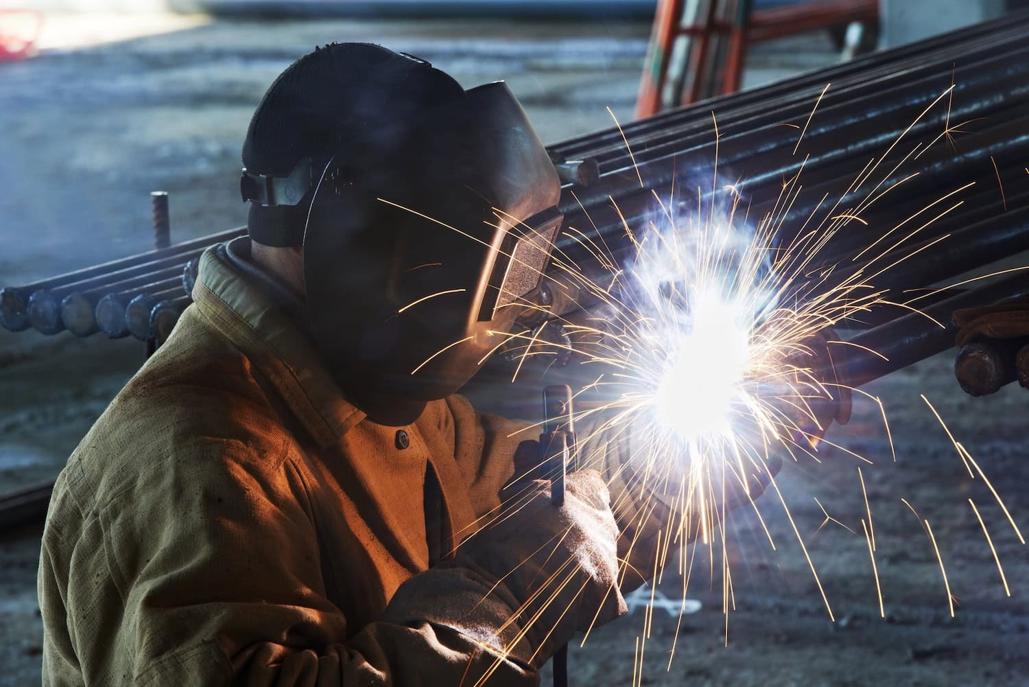 Person wearing protective gear welding metal with bright sparks.