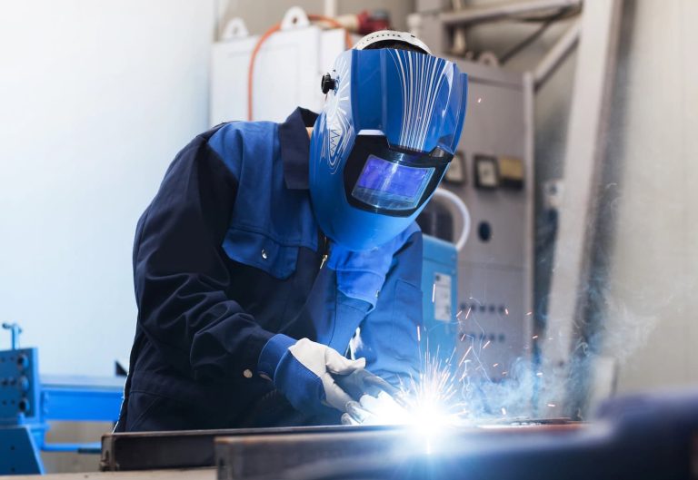 Person in protective gear welding metal, with sparks and bright light visible.
