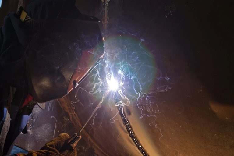 Close-up of a person welding metal, with sparks and light visible near the welding torch.