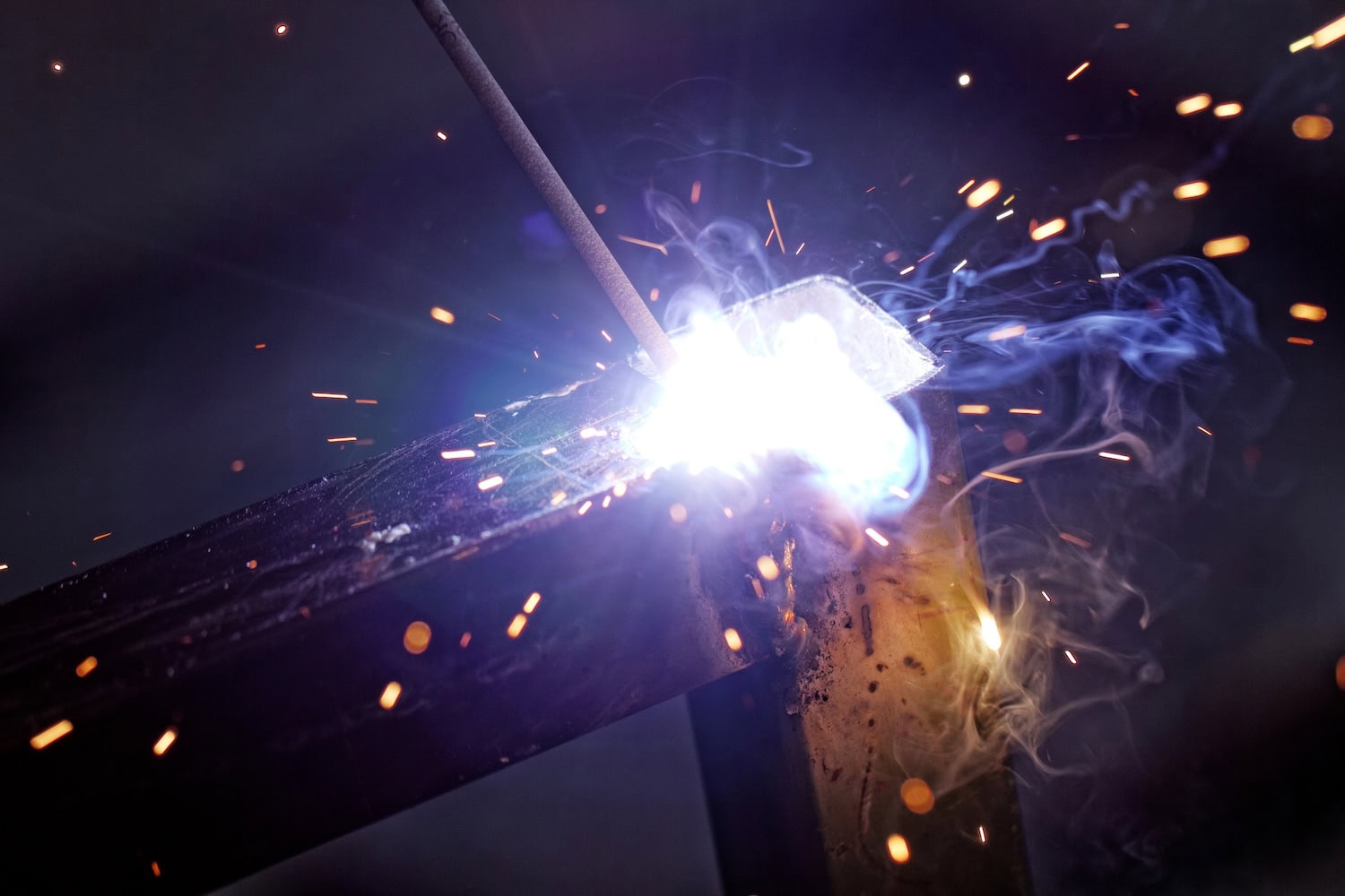 Close-up of welding process with bright sparks, smoke, and glowing metal.