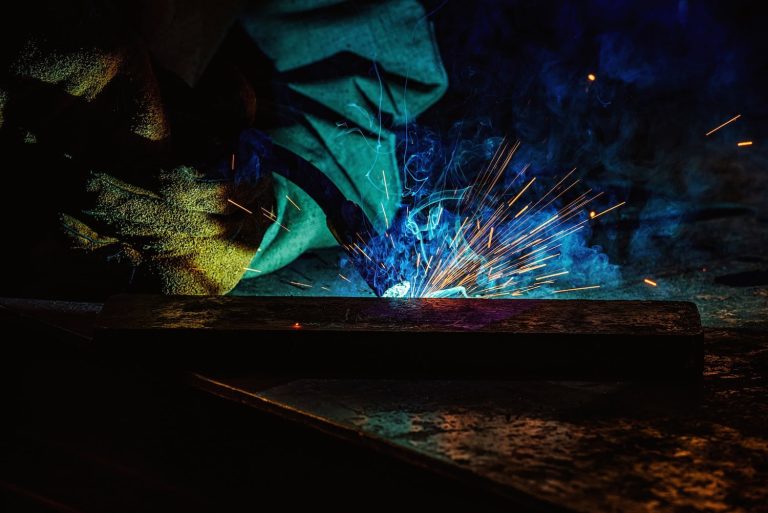 A person welding metal with bright sparks and blue smoke visible in a dark setting.
